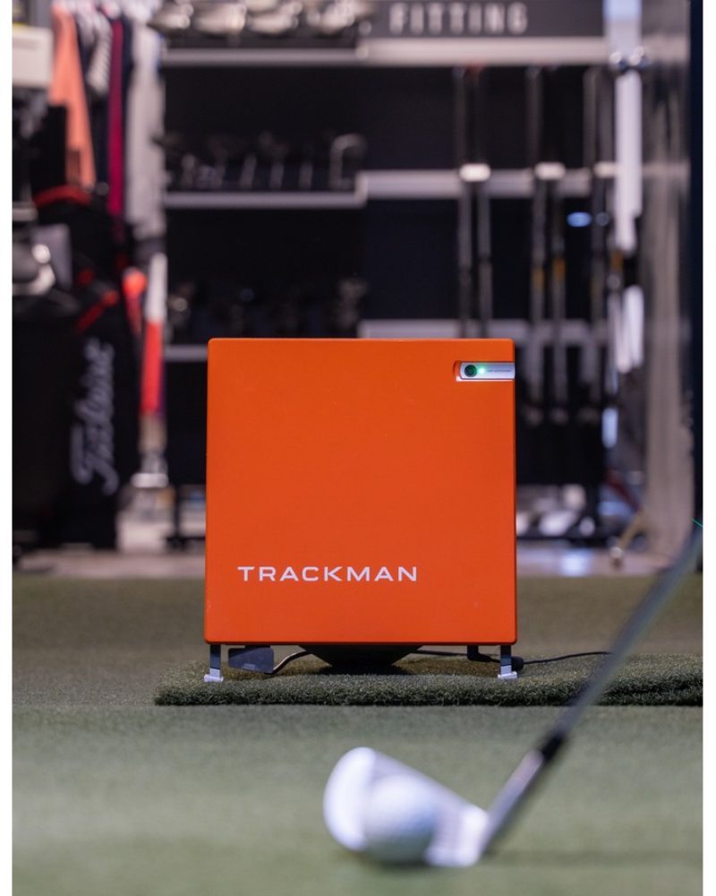 Orange Trackman device on a golf simulator with a golf club and ball in the foreground.